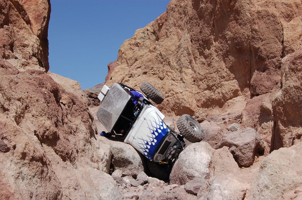 White off-road vehicle with blue flame decals tipped on its side in a rocky canyon