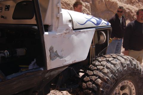 1985 Ford Bronco - Modified off-road vehicle with custom flame paint and large tires stands in a rocky, desert environment.