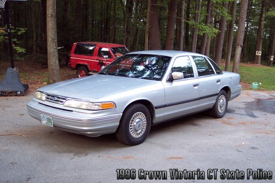 Silver sedan parked in a driveway with a red SUV behind it. Text on image says 1996 Crown Victoria CT State Police