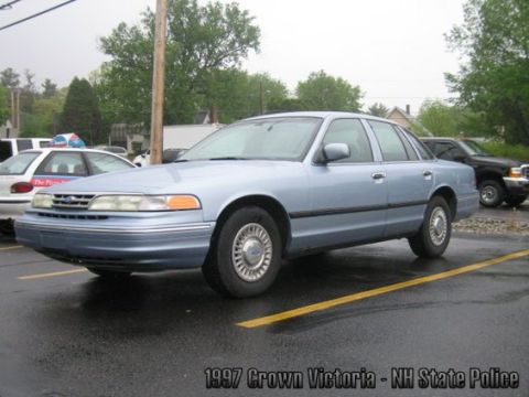 2001 Ford Crown Victoria - A light blue sedan is parked in a lot on a wet day. Other vehicles are visible in the background.