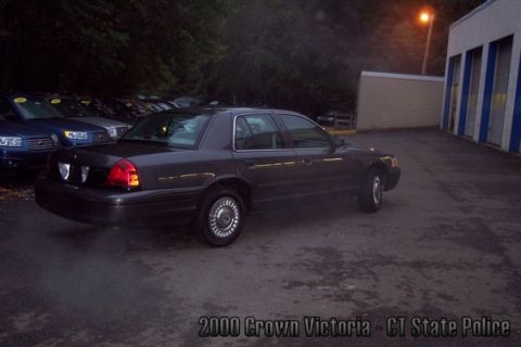 2001 Ford Crown Victoria - A dark sedan is parked in a lot at dusk, with other vehicles visible in the background.