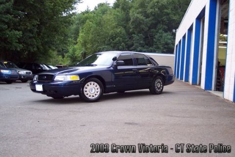 2001 Ford Crown Victoria - A dark blue 2003 Ford Crown Victoria sedan is parked outside a building with multiple garage bays.