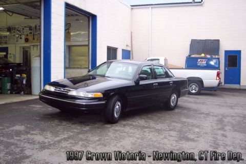 2001 Ford Crown Victoria - A black 1997 Crown Victoria sedan is parked in front of a garage, with a white pickup truck visible in the background.
