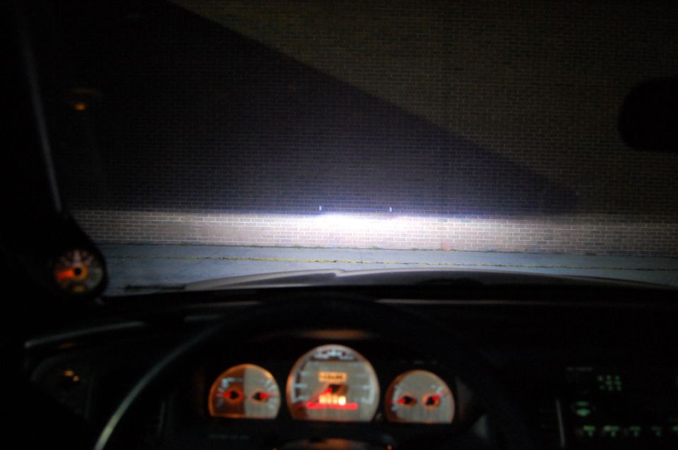 Night view from car interior showing lit gauges and headlights on a brick wall
