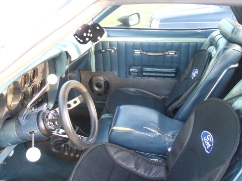 1974 Ford Ranchero - The interior of a 1974 Ford Ranchero features blue seats, a custom steering wheel, and fuzzy dice hanging from the mirror.