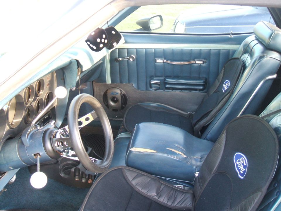 Interior of a 1974 Ford Ranchero with blue upholstery, racing seats, and fuzzy dice