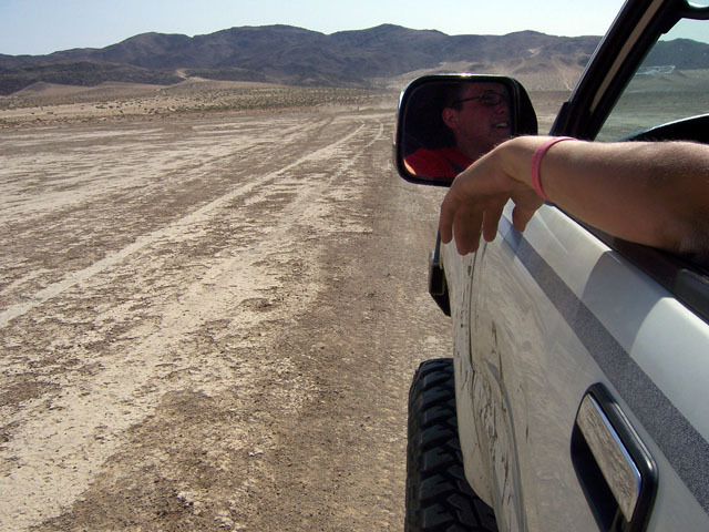 1993 Toyota 4Runner driving on a dirt road in a desert landscape. Person visible in side mirror