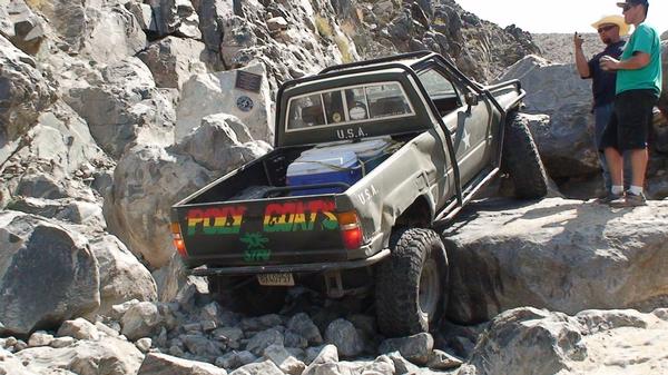 Olive green Toyota pickup truck with "PLAY GOATS" on tailgate, navigating rocky terrain