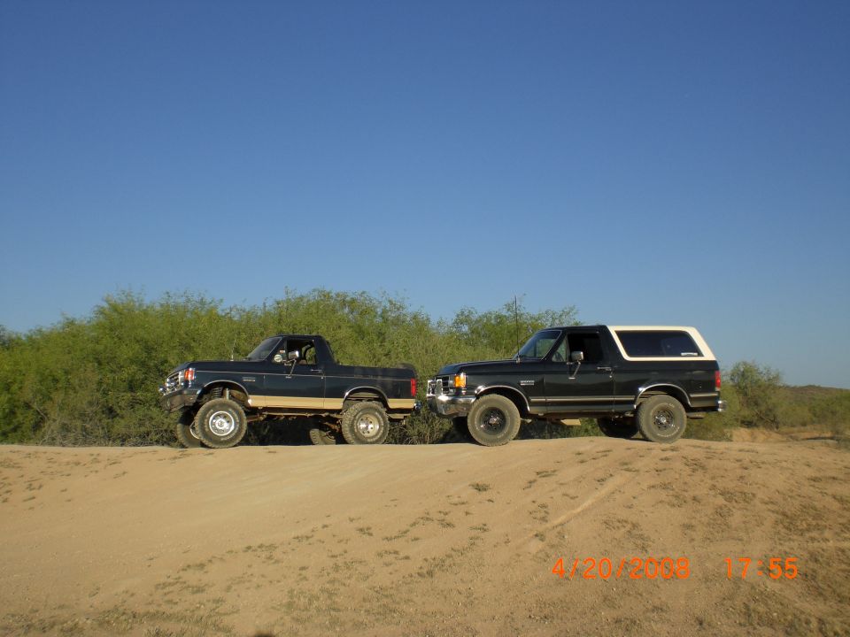 two Ford Broncos parked on a dirt hill, one is a pickup truck, the other is an SUV