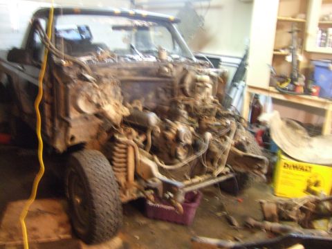 1989 Ford Bronco - The front end of a truck is shown disassembled in a workshop, with the engine and chassis components exposed.