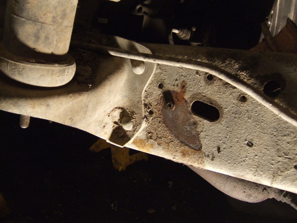 Rusty vehicle frame with suspension parts and exhaust pipe visible