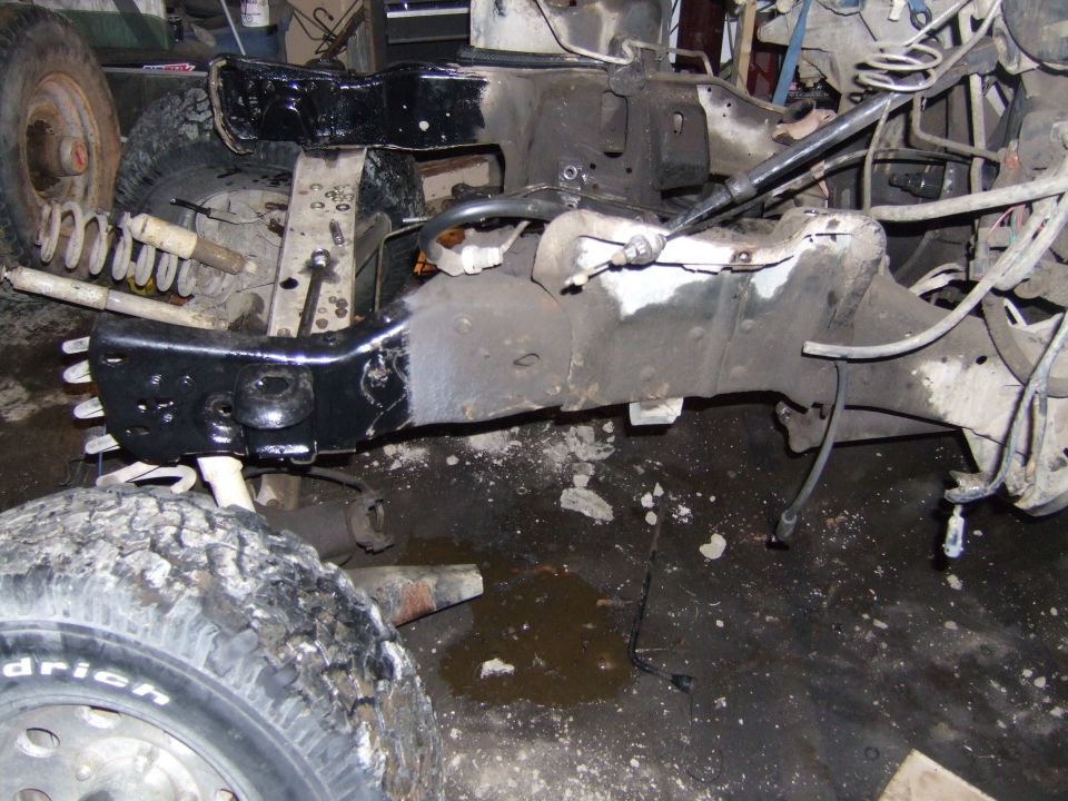 Close-up of a vehicle's frame and suspension parts, including a tire and shock absorber, in a workshop setting