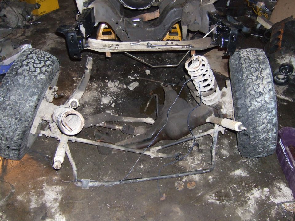Vehicle frame and suspension parts on a dirty floor, supported by yellow jack stands