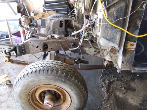 1989 Ford Bronco - The chassis and front suspension of a vehicle are shown, with extensive wiring and rusty metal parts.