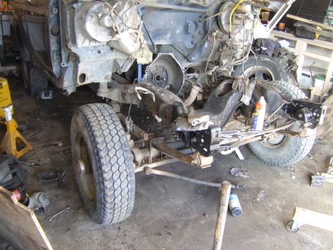 1989 Ford Bronco - A disassembled truck chassis sits on jack stands in a workshop, showing the frame and suspension components.