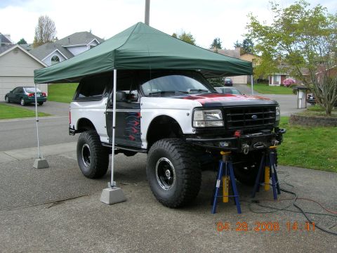 1996 Ford Bronco - A lifted 1996 Ford Bronco with custom bumper and flame decals is parked under a green canopy.