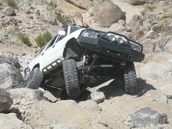 White 1993 Toyota 4Runner climbing rocks with aftermarket bumper and rock sliders