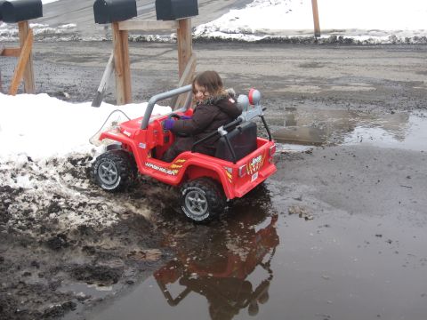 1990 Ford F-250 - A child drives a red toy Jeep Wrangler through a muddy area with snow.