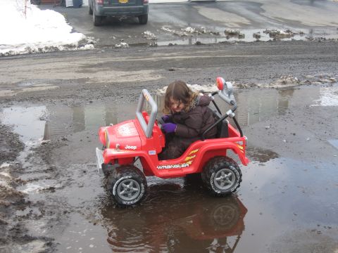 1990 Ford F-250 - A child drives a red toy Jeep Wrangler through puddles on a wet, muddy road.