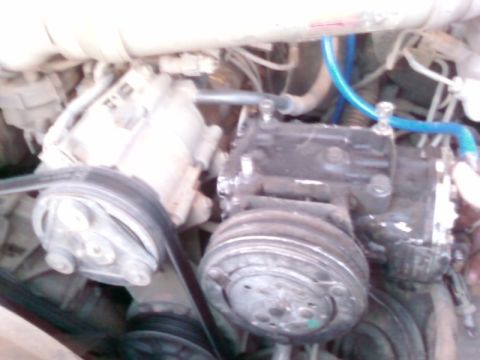 1995 Ford Bronco - Close-up view of engine components, belts, pulleys, and hoses, likely part of an air conditioning system.