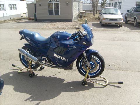 1988 Suzuki GSX600F Katana - A blue Suzuki motorcycle is parked on stands in front of a building with other vehicles in the background.
