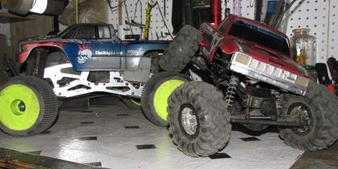 1999 Ford F-150 - Two custom remote control monster trucks are positioned side-by-side on a workbench.