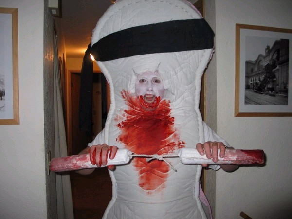 Person in a bloody tampon costume holding large tampons.