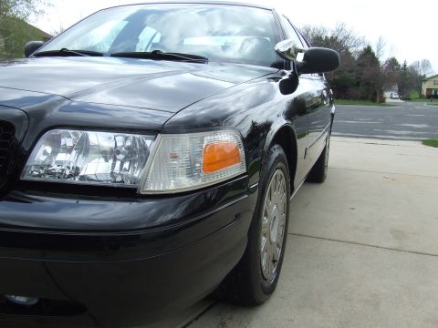 2003 Ford Crown Victoria - A close-up, low-angle shot of the front passenger side of a black Ford Crown Victoria. The vehicle is parked on a concrete driveway with a…