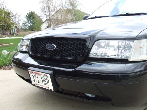 2003 Ford Crown Victoria - A close-up front view of a black Ford Crown Victoria's grille and headlights. A Wisconsin license plate with the text "371-HRP" is mounted…