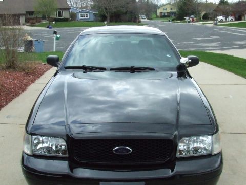 2003 Ford Crown Victoria - Front view of a black 2003 Ford Crown Victoria parked on a concrete driveway. The car has a black grille and clear headlights, with a spotl…