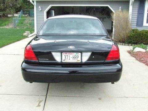 2003 Ford Crown Victoria - The rear view of a black 2003 Ford Crown Victoria is shown parked in a driveway in front of a garage. The vehicle has a Wisconsin license p…
