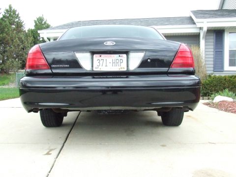 2003 Ford Crown Victoria - The rear view of a black Ford Crown Victoria is shown parked on a concrete driveway in front of a house. The license plate reads "371-HRP"…