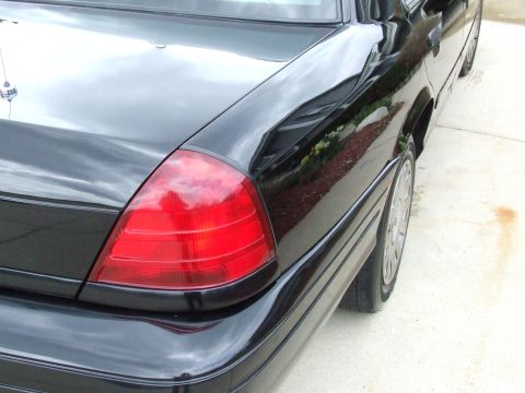 2003 Ford Crown Victoria - The rear passenger side of a black Ford Crown Victoria is shown, reflecting the surroundings in its glossy paint. The red taillight and chr…