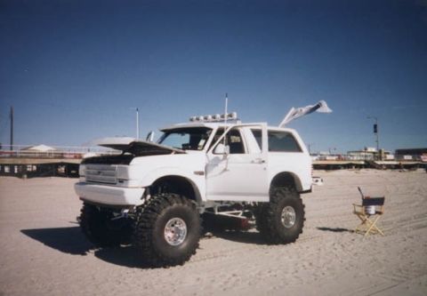 1981 Ford Bronco - This lifted Ford Bronco is parked on a beach with its hood open under a clear blue sky.