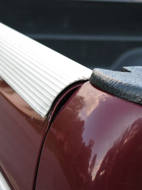 1991 Ford F-150 - Close-up view of the bed rail of a maroon pickup truck, showing a white ribbed trim piece and a textured black cap. The paint shows reflect…