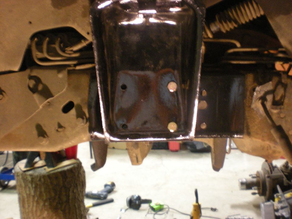 Underside of a vehicle frame with black painted brackets and visible rust.