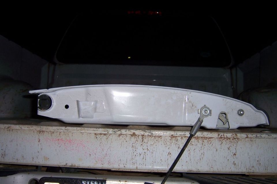 White tailgate handle assembly with black cable, mounted on a rusty surface.