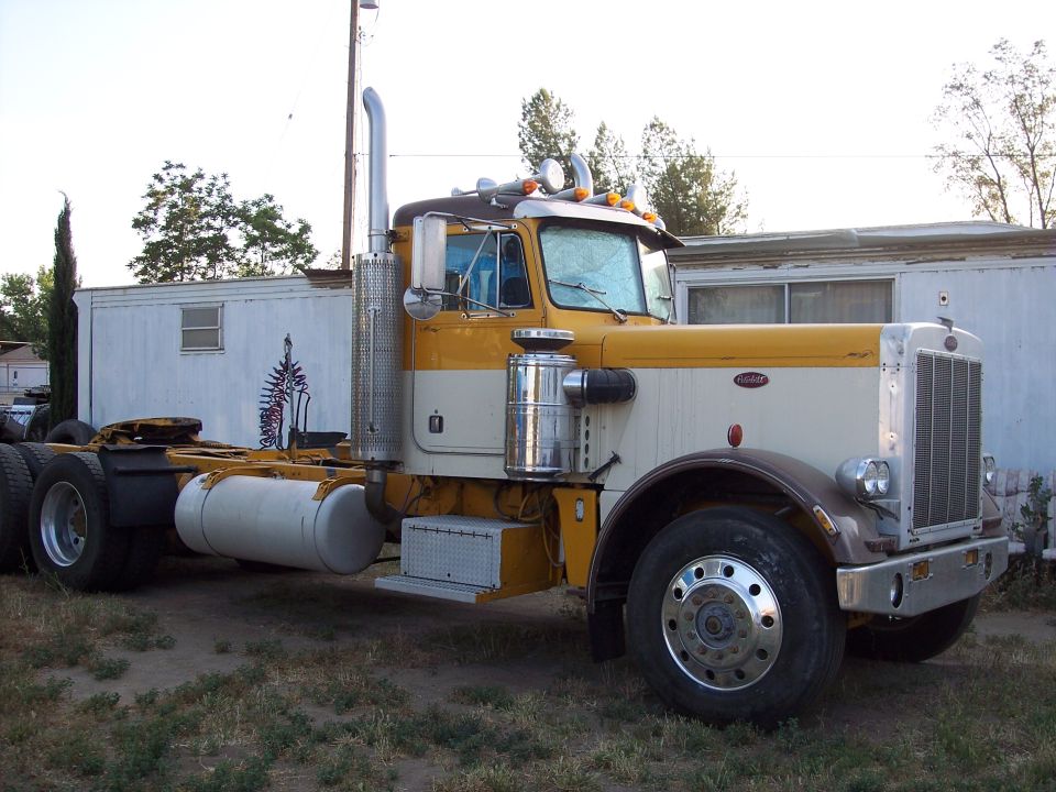 Yellow and cream semi-truck with chrome stacks parked in front of a trailer.