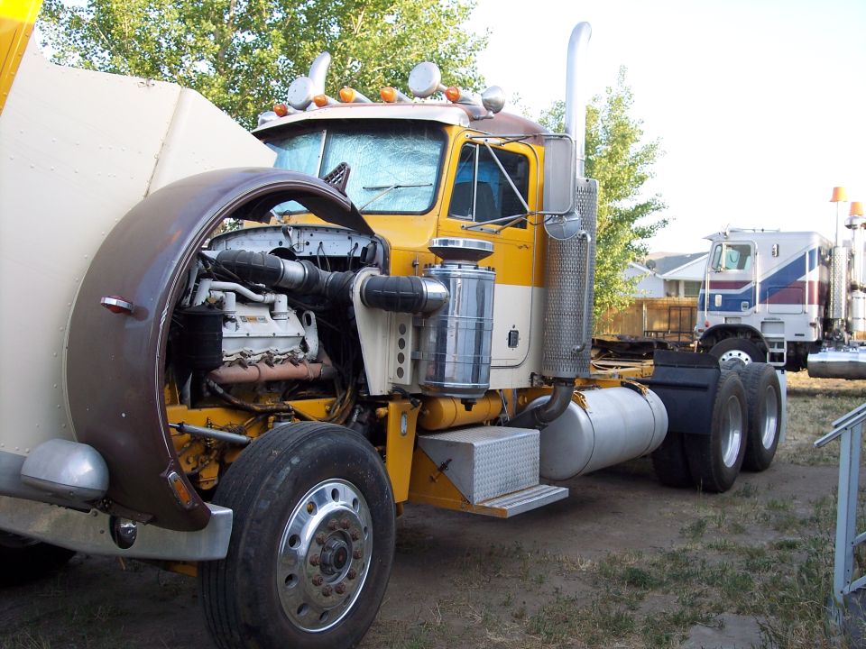 Yellow and brown semi-truck with hood open, engine visible. Another semi-truck in background.