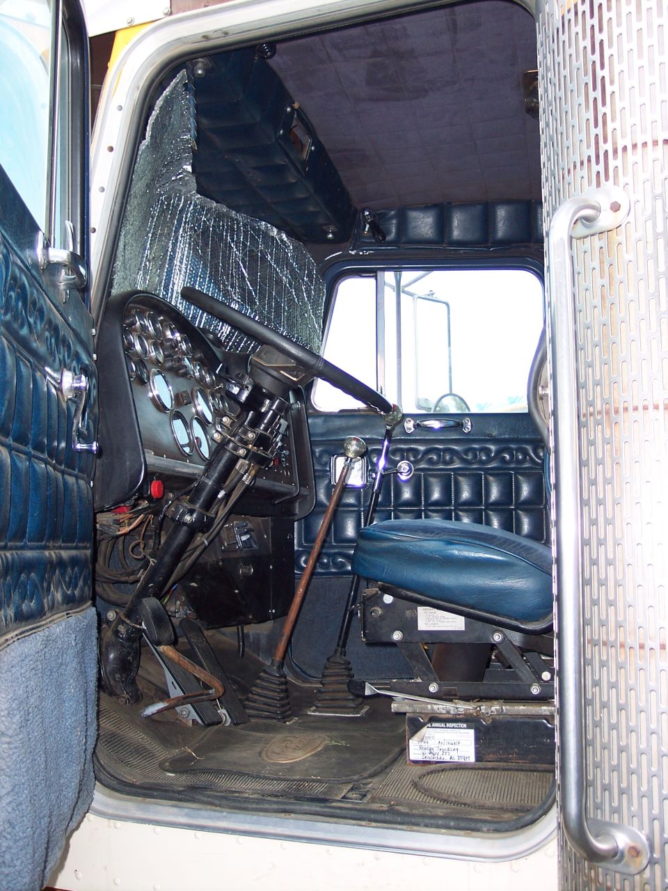 Interior view of a vintage truck cab, showing dashboard, steering wheel, seat, and door.