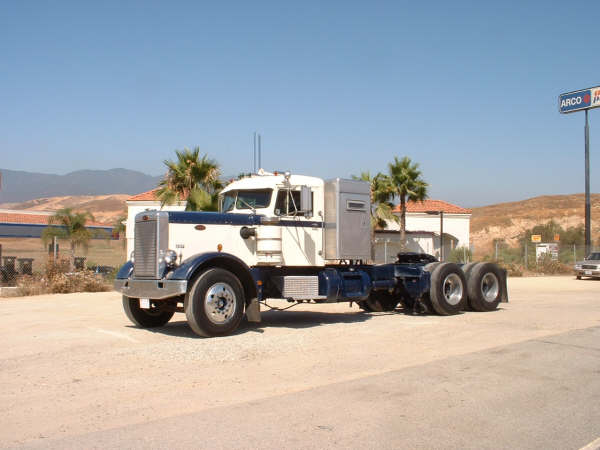 Classic white-and-blue long-nose conventional semi tractor parked bobtail near palm trees and an ARCO sign