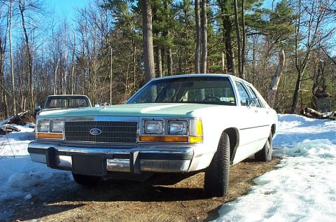 2001 Ford Crown Victoria - A white sedan with a distinctive light blue grille sits in a snowy landscape, with another vehicle partially visible behind it.