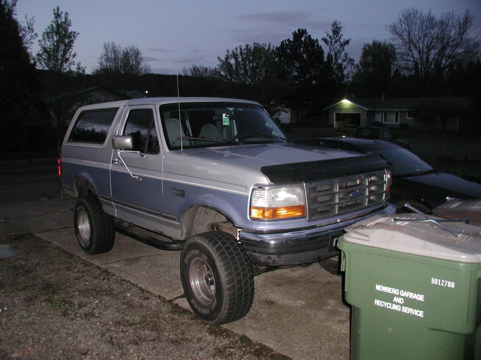 Lifted two-tone silver and blue Ford Bronco SUV at dusk in a driveway, front three-quarter view