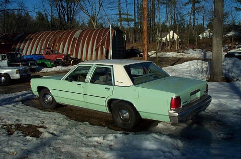 2001 Ford Crown Victoria - A light green sedan with a white roof sits in a snowy lot next to a large Quonset hut.