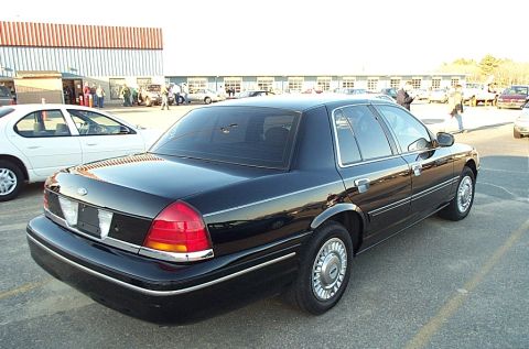 2001 Ford Crown Victoria - A black 2001 Ford Crown Victoria is parked in a lot next to a white sedan.
