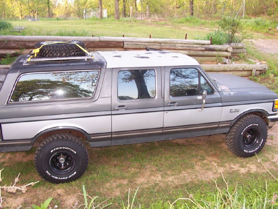 Gray and silver extended cab pickup truck with spare tire on roof rack, parked outdoors.