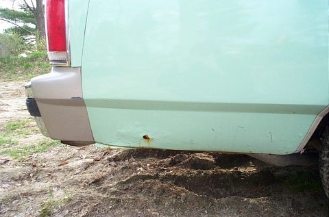 2001 Ford Crown Victoria - Close-up of the rear lower body panel and quarter of a pale green vehicle with red taillight, parked on bare dirt.