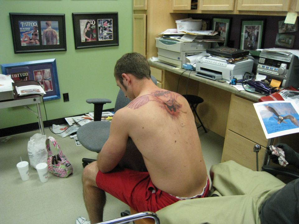 Person in a tattoo parlor with a large tattoo on their back, facing away from the camera.