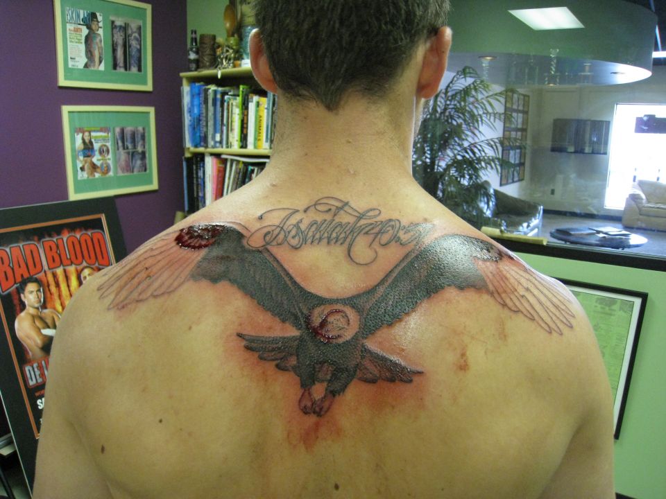 Large eagle tattoo with banner across a man's upper back in a tattoo studio