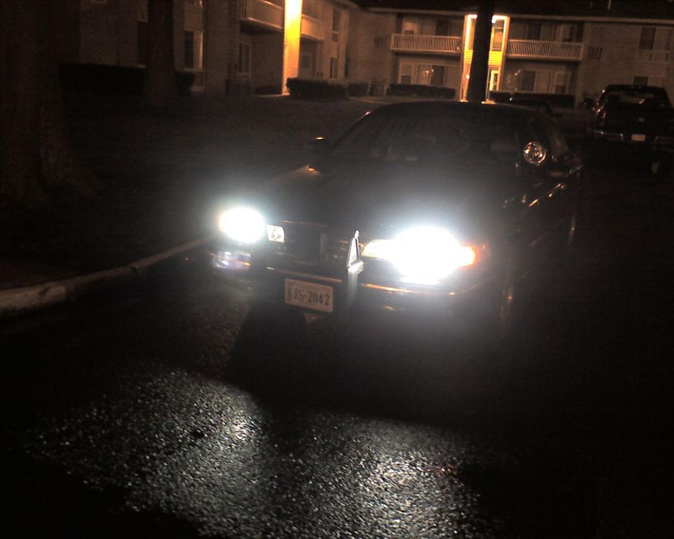 Dark sedan at night with headlights on, front plate KJS-2042, in an apartment parking lot